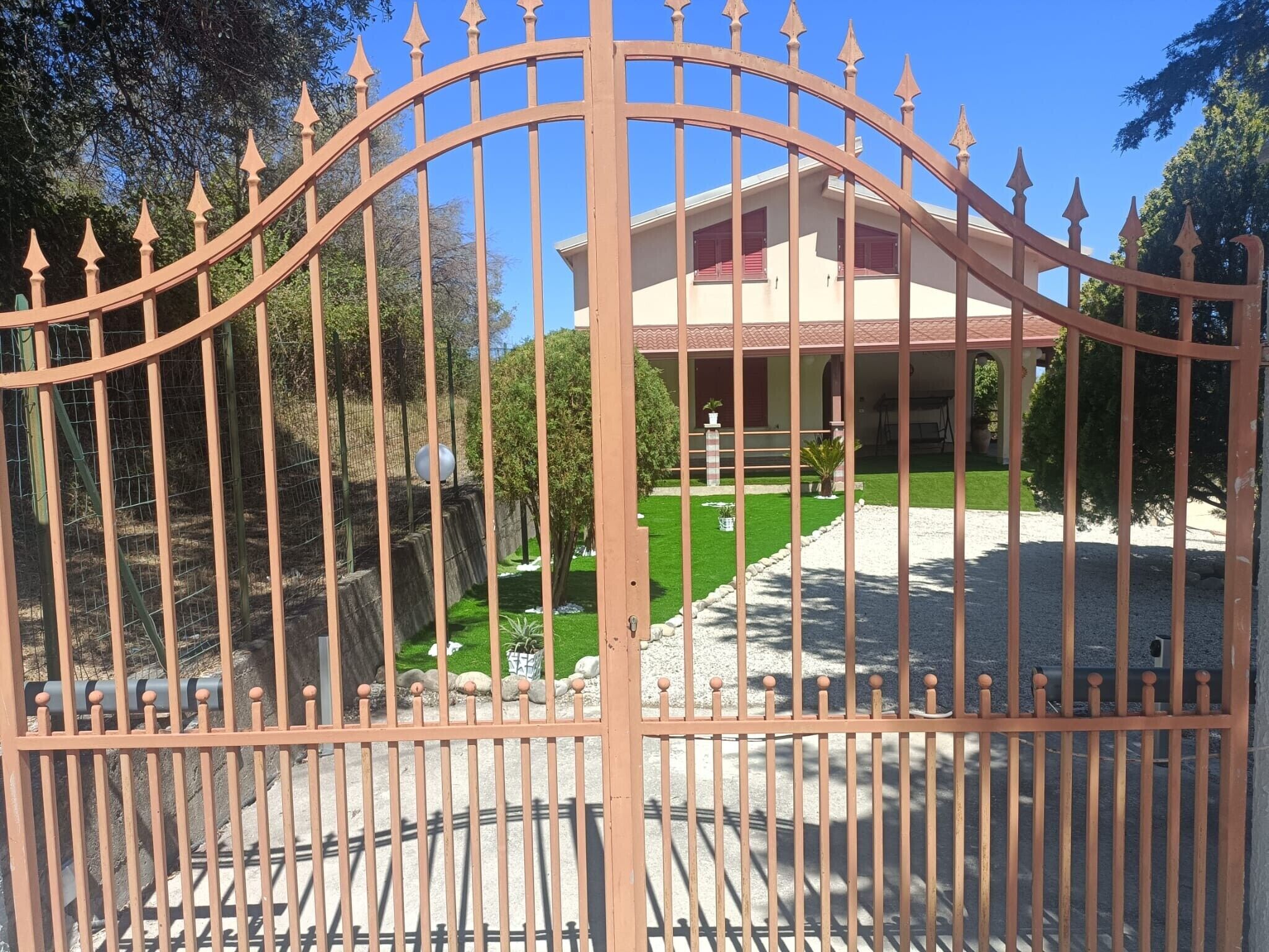 A gated entrance with a curved top, a well-maintained lawn, and a building with a red roof and beige walls.