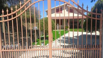 A gated entrance with a curved top, a well-maintained lawn, and a building with a red roof and beige walls.