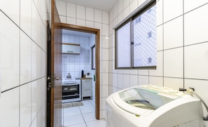 A compact kitchen with white tiles, a built-in oven, and a window with a mesh screen.