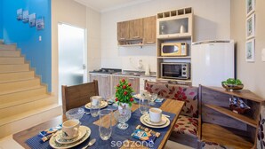 A modern kitchen with wooden cabinets, a microwave, and a refrigerator. There is a dining table set with plates, cups, and a vase of flowers. - Casa 2Q c/ churrasq. 600m orla MCA0609 (Picarras)