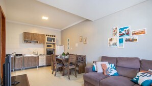 A modern living room with a brown sofa and a dining area with wooden chairs and a table. - Casa 2Q c/ churrasq. 600m orla MCA0609 (Picarras)