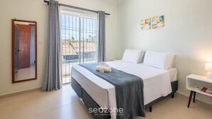 A bedroom with a bed, a bedside table, a window with curtains, and a view of the outside. - Casa 2Q c/ churrasq. 600m orla MCA0609 (Picarras)