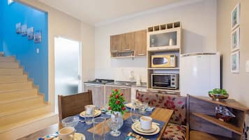 Una cocina moderna con armarios de madera, un microondas y un refrigerador. Hay una mesa de comedor con platos, tazas y un jarrón de flores.
