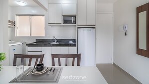 A modern kitchen with white cabinets, a microwave, a refrigerator, and a dining area with a table and chairs. - Modern Apartment Near the BC Ferris Wheel Mbh0601 (Balneário Camboriú)