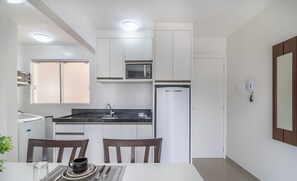 Una cocina moderna con armarios blancos, microondas, refrigerador y un comedor con mesa y sillas.