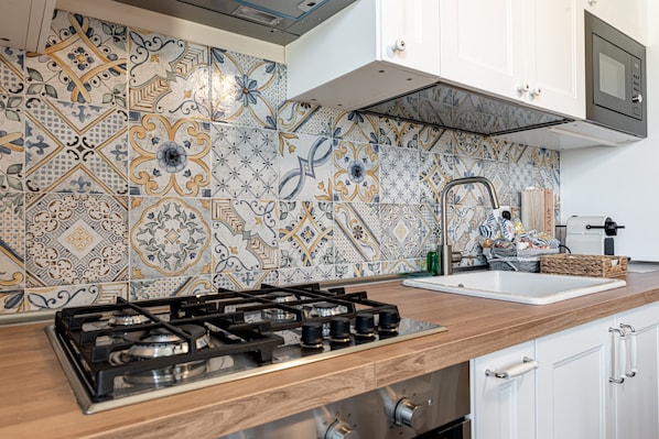 Une cuisine équipée d’une cuisinière à gaz, de meubles blancs, d’un four à micro-ondes et d’un plan de travail recouvert de carreaux.