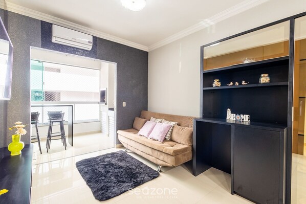 Una sala de estar moderna con un sofá color beige, un tapete negro y un estante negro con objetos decorativos.