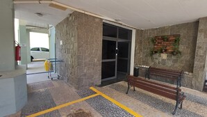 A lobby with a stone wall, a bench, a fire extinguisher, and a yellow trash bin. - Studio Cambuí 67 - Community Center (Campinas)