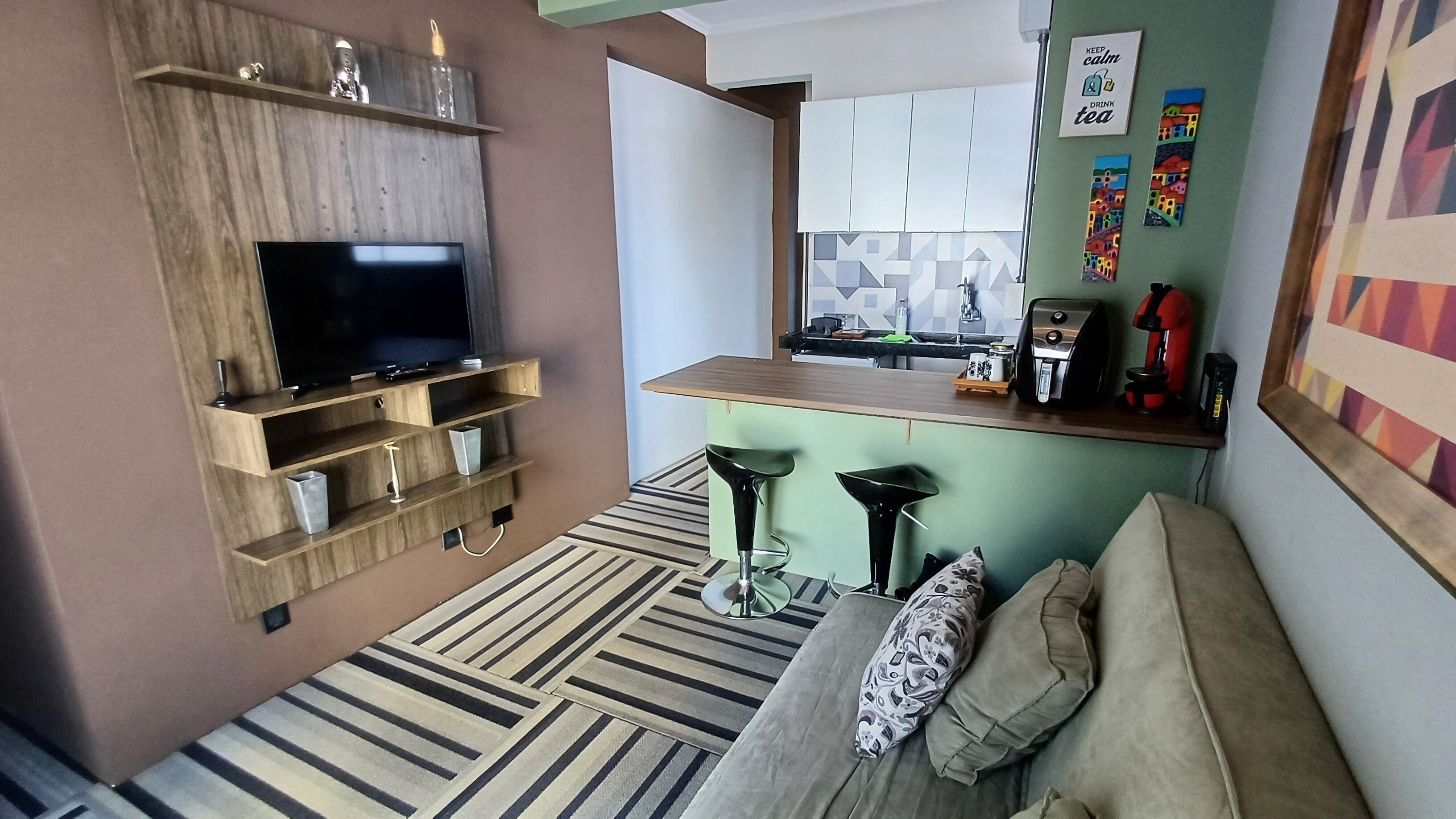 Een compacte woonruimte met een flatscreen televisie, een kitchenette, een bank en een gestreept tapijt.