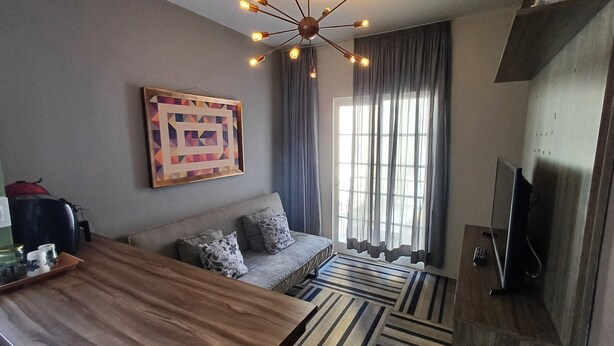 A modern living room with a sofa, a coffee table, a TV, and a geometric painting on the wall. - Studio Cambuí 67 - Community Center (Campinas)