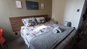 A neatly made bed with a newspaper print bedspread, a wooden headboard, and a bedside table with a lamp and a book. - Studio Cambuí 67 - Community Center (Campinas)