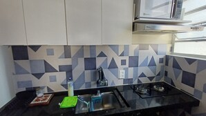A kitchen with a black countertop, a gas stove, a microwave, and a patterned backsplash. - Studio Cambuí 67 - Community Center (Campinas)