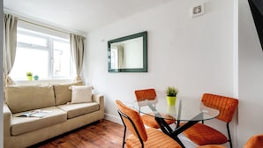 A modern living room with a sofa, a glass-top dining table, and orange chairs. - 2 Bedroom flat in Putney by the river (London)