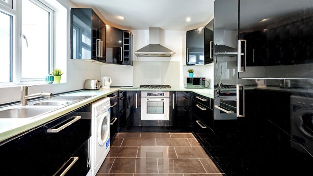 A modern kitchen with black cabinets, stainless steel appliances, a built-in oven, and a washing machine. - 2 Bedroom flat in Putney by the river (London)