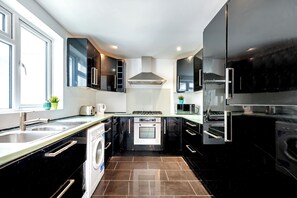 Une cuisine moderne avec des meubles de couleur noire, des appareils électroménagers en acier inoxydable, un four encastré et un lave-linge.