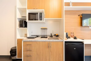 A compact kitchen with wooden cabinets, a microwave, a sink, and a black dishwasher. - Charming studio in São Caetano ap111 (São Caetano do Sul)