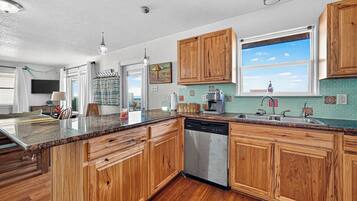 Una cocina con armarios de madera, lavavajillas, ventana con vistas y encimera con diversos objetos.
