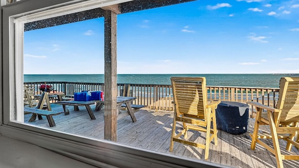 Eine Holzterrasse mit Sitzgelegenheiten im Freien, mit Blick auf Strand und Meer.