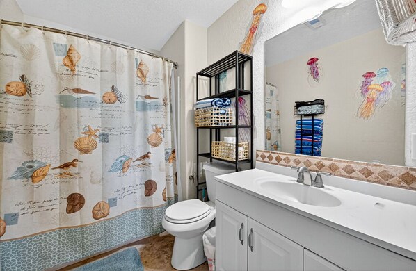 A bathroom with a shower curtain featuring sea creatures, a white toilet, a white sink with a mirror, and a tiled backsplash.