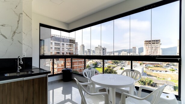 A modern balcony with a city view, a round table, white chairs, and a kitchen area with a sink and cabinets. - Cozy Apt 550m From the Beach in Porto Belo Lnb502 (Porto Belo)