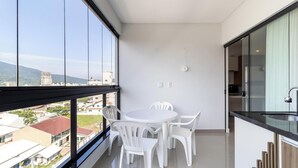 A modern balcony with a white table and chairs, a kitchen area, and a view of buildings and mountains. - Cozy Apt 550m From the Beach in Porto Belo Lnb502 (Porto Belo)