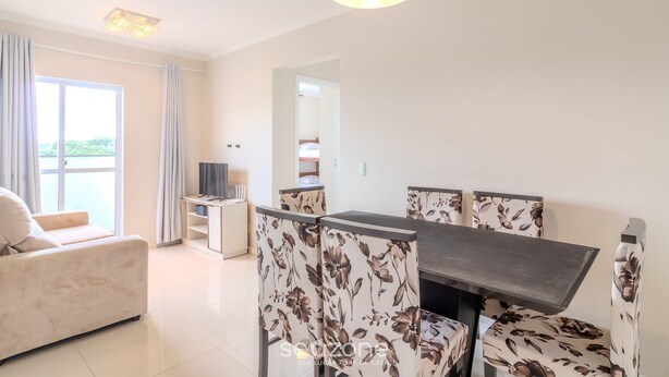 A modern living room with a sofa, a dining table with floral chairs, a TV, and a balcony with curtains. - Building With a Pool 400m From Beach - LEA (Picarras)