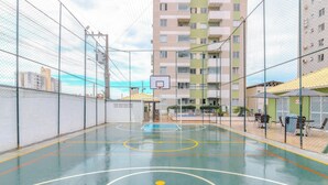 An indoor basketball court with a blue and yellow boundary line, surrounded by a chain-link fence and a building in the background. - Building With a Pool 400m From Beach - LEA (Picarras)