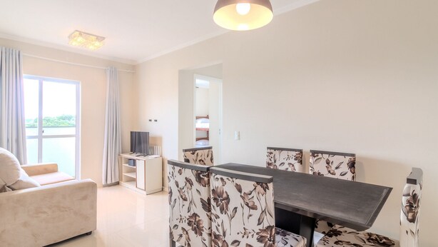 A modern living room with a sofa, a dining table with floral chairs, a TV, and a balcony with curtains. - Building With a Pool 400m From Beach - LEA (Picarras)