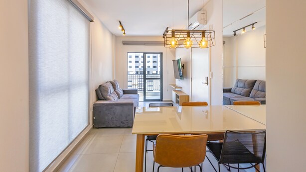 A modern living room with a sofa, a dining table, and a TV mounted on the wall.