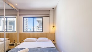 A modern hotel room with a large bed, a bedside table with a phone, and a window with a city view.