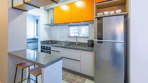 A modern kitchen with stainless steel appliances, wooden bar stools, and orange cabinetry.