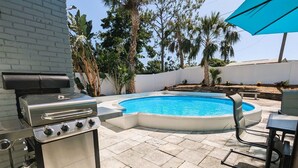 A backyard with a swimming pool, a barbecue grill, and outdoor seating.