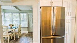 A kitchen with a stainless steel refrigerator, white cabinets, and a dining area with a table and chairs.