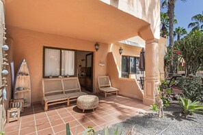 An outdoor patio with wicker furniture, a small round ottoman, and a view of the interior through a glass door. - 'Blanca del Sol Oasis Duna' Holiday with Shared Pool, Private Terrace and Wi-Fi (Corralejo)
