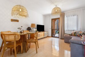 A modern living room with a dining area, a flat-screen TV, wicker lamps, and a sofa with decorative pillows. - 'Blanca del Sol Oasis Duna' Holiday with Shared Pool, Private Terrace and Wi-Fi (Corralejo)