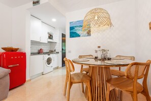 Una cocina moderna con armarios blancos, un refrigerador rojo y una zona de comedor con una mesa redonda y sillas de madera.