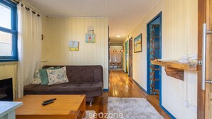 Una sala de estar acogedora con un sofá marrón, una mesa de centro de madera y una alfombra blanca. Se ve una ventana con cortinas, una chimenea y un pasillo que conduce a otra habitación.