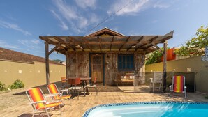 Una casa de madera con un porche cubierto, piscina y mobiliario de exterior.