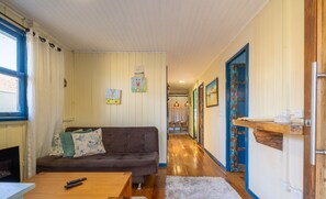A cozy living room with a brown sofa, a wooden coffee table, and a white rug. There is a window with curtains, a fireplace, and a hallway leading to another room. - 5BR House w/ Pool Near Beto Carrero SC Jrs0045 (Penha)