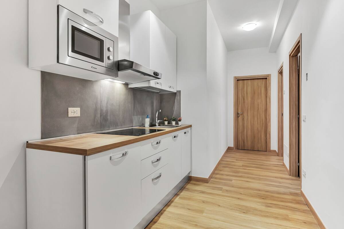 Uma cozinha moderna com armários brancos, bancada de madeira e micro-ondas embutido.