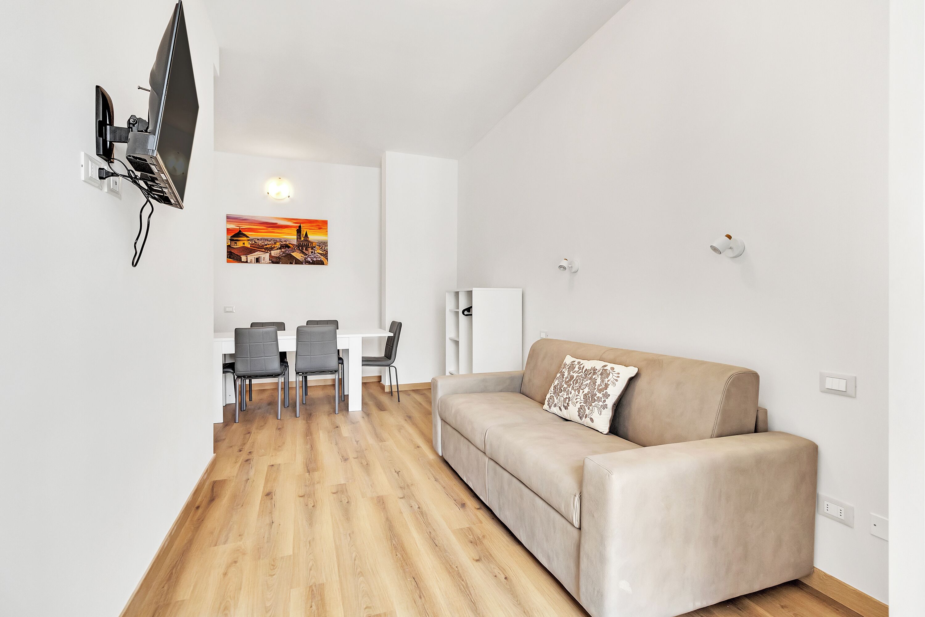 A modern living room with a sofa, a dining area with chairs, and a mounted TV.