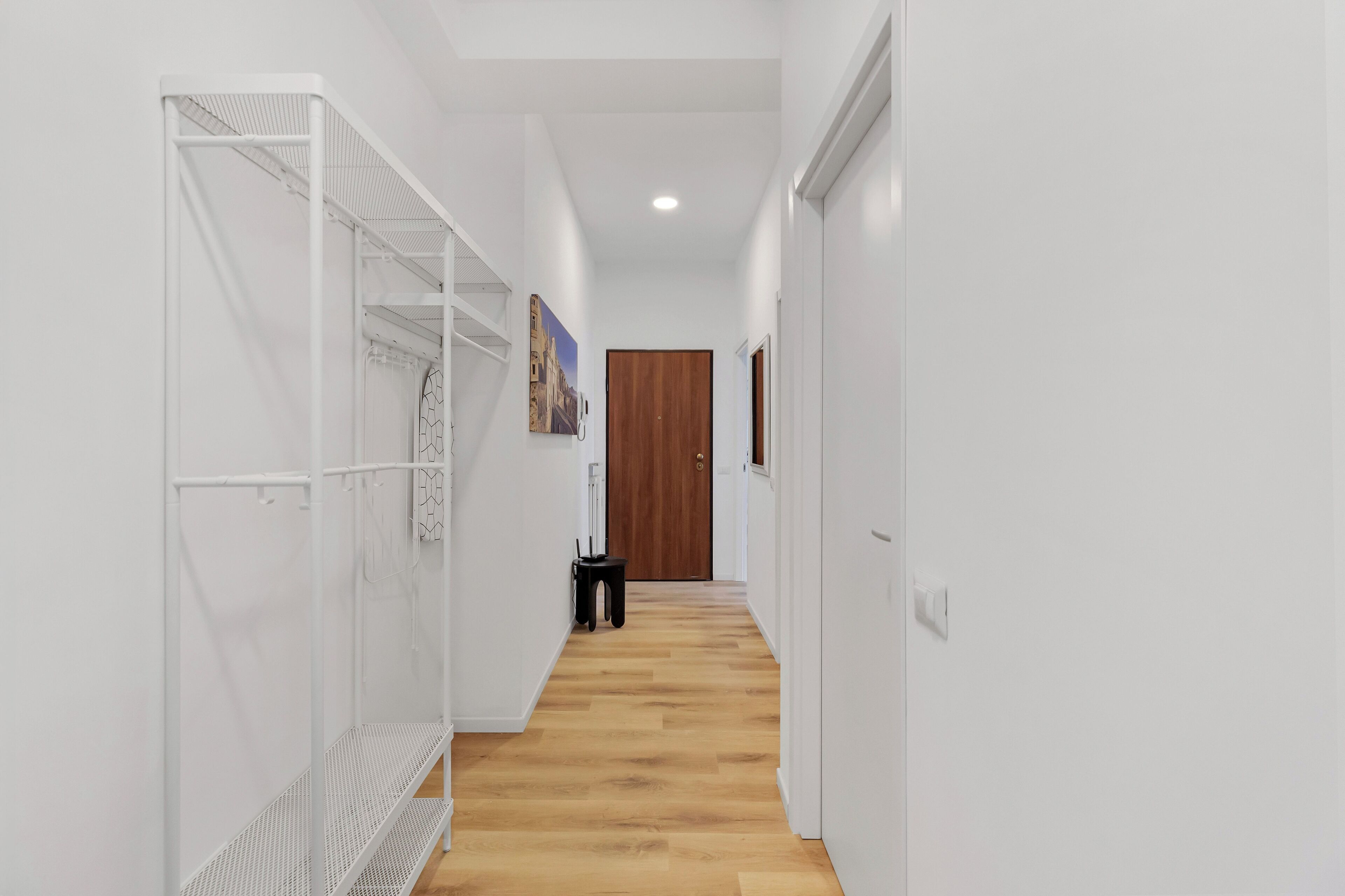Un pasillo estrecho con paredes blancas y suelo de madera, que conduce a una puerta de madera al final.