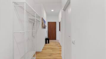 Un pasillo estrecho con paredes blancas y suelo de madera, que conduce a una puerta de madera al final.