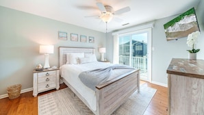 A bedroom with a bed, nightstands, a ceiling fan, a large window, and a view of a building outside. - Gold Coast 3BR Condo / Decks, Parking, Walk to Beach (Ocean City)