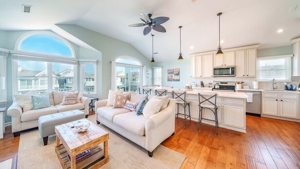 A spacious living room with a large window, a dining area, and a kitchen with white cabinets and a microwave. - Gold Coast 3BR Condo / Decks, Parking, Walk to Beach (Ocean City)