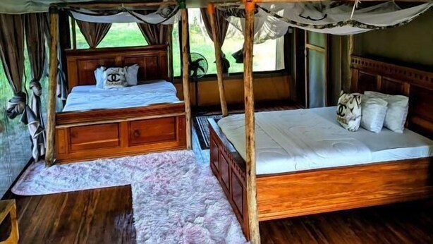 Une pièce aménagée en tente, avec deux lits en bois, chacun recouvert d’une literie blanche et agrémenté d’oreillers, et un petit tapis sur le sol.