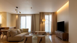 Ein modernes Wohnzimmer mit einer Couch, Hocker, einem Couchtisch, einem Fernseher und einem Essbereich mit Tisch und Stühlen.