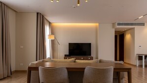 Ein modernes Wohnzimmer mit einem Holzesstisch, zwei Sesseln, einem Flachbildfernseher und einer Stehlampe.