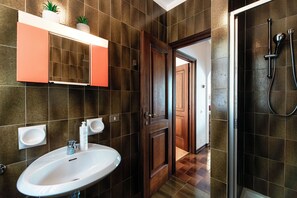 A bathroom with a white sink, two wall-mounted basins, a wooden door, and a shower area.