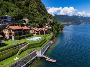 A lakeside hotel with a swimming pool, a dock, and a mountain backdrop. - Musso Waterside (Musso)